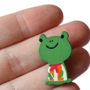 May include: A green wooden frog with a painted smile and orange and white striped shirt.