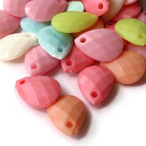 May include: Assortment of colorful teardrop-shaped beads with a hole at the top. The beads are made of plastic and come in shades of pink, peach, yellow, and blue.