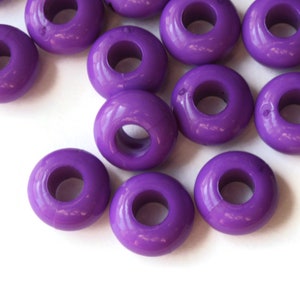 May include: A group of purple plastic beads with a hole in the center. The beads are scattered on a white surface.