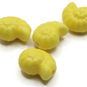 May include: Four yellow ceramic seashell beads. Each bead has a spiral design and a hole for stringing. The beads are a bright, glossy yellow color and are suitable for jewelry making or other craft projects.