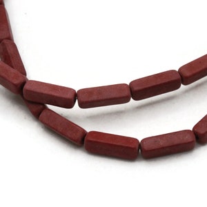May include: A strand of dark red rectangular beads. The beads are made of a rough, textured material.