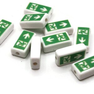 May include: A collection of white rectangular beads with green emergency exit symbols. Each bead has a hole for stringing. The green symbols include a running person and an arrow indicating the direction of the exit.