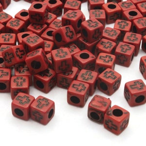 May include: A pile of red cube-shaped beads with a black cross design. The beads have a hole through the center for stringing.