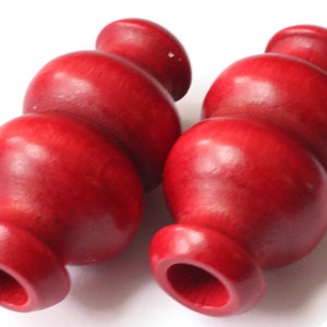 Może przedstawiać: Dwa czerwone drewniane koraliki o kształcie przypominającym żarówkę. Koraliki mają gładkie, polerowane wykończenie.