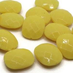 May include: A group of 12 yellow oval-shaped glass beads. The beads have a smooth, glossy finish.