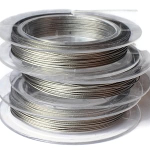 May include: A spool of silver-colored wire wound around a clear plastic spool. The spool is stacked on top of two other spools, all of which are clear plastic.