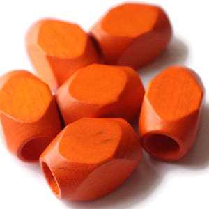 May include: Six orange wooden beads with a faceted, geometric shape. The beads are smooth and have a glossy finish.