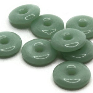May include: Eight green jade donut beads with a hole in the center. The beads are smooth and polished.