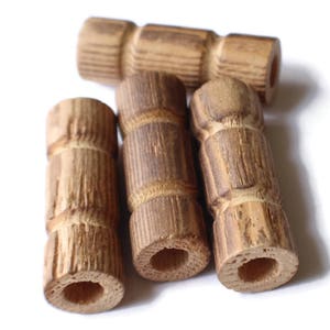 Puede incluir: Cuatro pomos de madera con un patrón de rayas marrones y marrón claro. Los pomos tienen una forma cilíndrica con una parte superior e inferior redondeadas.