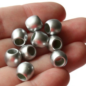 May include: A close-up of a hand holding a group of silver round beads with a hole in the center. The beads are smooth and shiny.