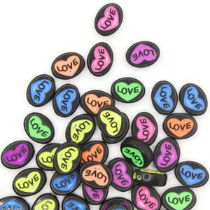 May include: A collection of black oval-shaped beads with a heart design and the word "LOVE" in various colors, including pink, orange, green, and blue. The beads are scattered on a white surface.