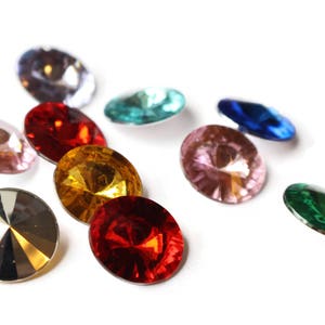 May include: Assortment of colorful, faceted glass gems in various shapes and sizes. The gems are arranged on a white background.