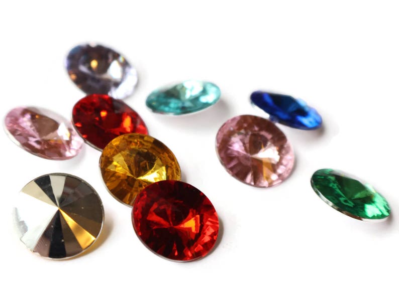 May include: Assortment of colorful, faceted glass gems in various shapes and sizes. The gems are arranged on a white background.