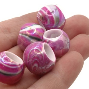 Pode incluir: Seis contas rosa e brancas com um padrão de redemoinho e um acabamento brilhante. As contas têm um furo central e são seguradas em uma mão sobre um fundo branco. Cada conta tem aproximadamente 1,9 cm de diâmetro.