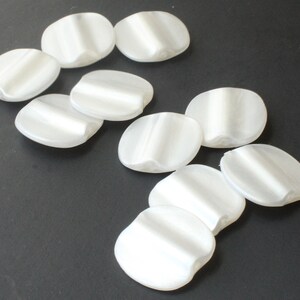 May include: Ten white plastic buttons with a raised design. The buttons are oval shaped and have a smooth, glossy finish.