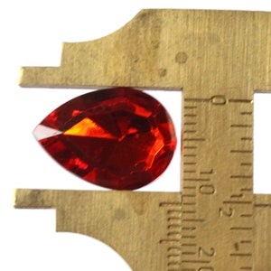 May include: A red teardrop-shaped crystal measuring approximately 1.5 inches in length.
