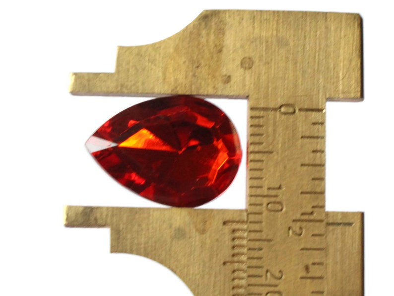 May include: A red teardrop-shaped crystal measuring approximately 1.5 inches in length.