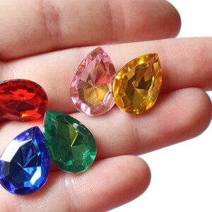 May include: Five teardrop-shaped faceted glass rhinestones in various colors: red, pink, yellow, green, and blue.