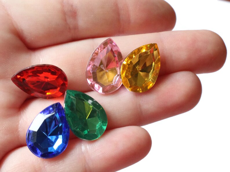 May include: Five teardrop-shaped faceted glass rhinestones in various colors: red, pink, yellow, green, and blue.