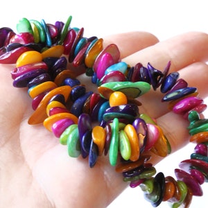 May include: A colorful bracelet made of iridescent, polished shell pieces. The bracelet features a variety of colors, including orange, yellow, green, blue, and purple. The shell pieces are strung together to form a flexible, eye-catching accessory.