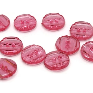 以下が含まれることがあります： テクスチャ加工が施されたストライプ模様のピンク色のプラスチックボタンが10個。ボタンにはそれぞれ2つの穴があります。