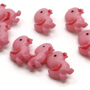May include: Eight pink plastic buttons shaped like chicks. Each chick has a red wing design and black eyes.