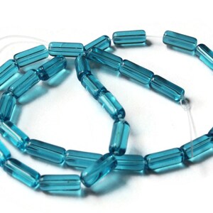 Peut inclure: Un brin de perles en verre bleu turquoise, chaque perle est un long cylindre avec un bord légèrement arrondi. Les perles sont enfilées sur un cordon élastique transparent.