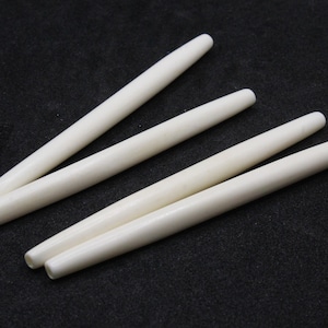 May include: Four white bone-like sticks, each with a rounded end, are arranged in a staggered pattern on a black surface.