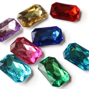 May include: Assortment of eight faceted glass gems in various colors, including purple, red, yellow, blue, pink, teal, and green. The gems are rectangular in shape and have a glossy finish.