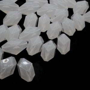 Puede incluir: Un montón de cuentas de vidrio blancas y facetadas. Las cuentas son translúcidas y tienen un ligero brillo iridiscente.