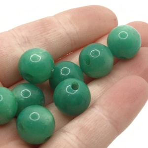 May include: A collection of eight green glass beads, each with a smooth, shiny surface. The beads are round and appear to be made of a translucent material.