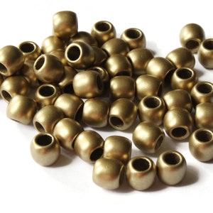 May include: A group of gold-colored round beads, with a smooth, matte finish. The beads are scattered on a white surface.