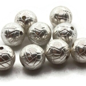 May include: A group of silver-coloured round beads with a textured surface. The beads have a hole through the centre for stringing.