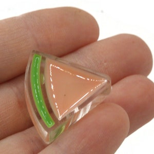 Puede incluir: Un amuleto de vidrio en forma de rodaja de sandía con cáscara verde y pulpa rosa.
