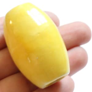 May include: A smooth, yellow ceramic bead with a glossy finish. The bead is oval-shaped and has a hole drilled through the center.