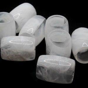 May include: A collection of white, marbled glass beads in various shapes. The beads include cylindrical and rectangular forms, with a translucent, swirling pattern. The objects are arranged against a black background.