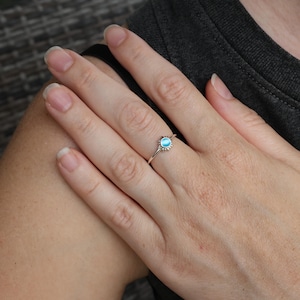 May include: A silver ring with a light blue stone set in a sunburst design.
