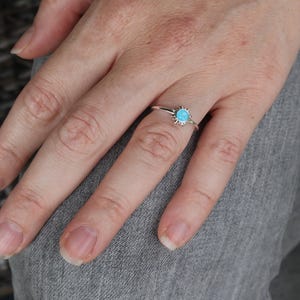 May include: A silver ring with a turquoise stone set in a sunburst design.