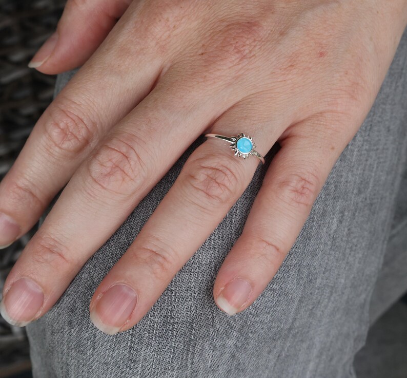 May include: A silver ring with a turquoise stone set in a sunburst design.