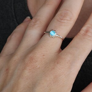 May include: A silver ring with a blue gemstone in the center, surrounded by a sunburst design.