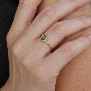 May include: A gold ring with a green gemstone set in a sunburst design.