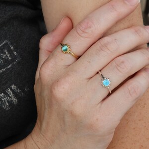 May include: Two rings with a sun design and a turquoise stone. The ring on the left has a gold band and a green stone. The ring on the right has a silver band and a blue stone.