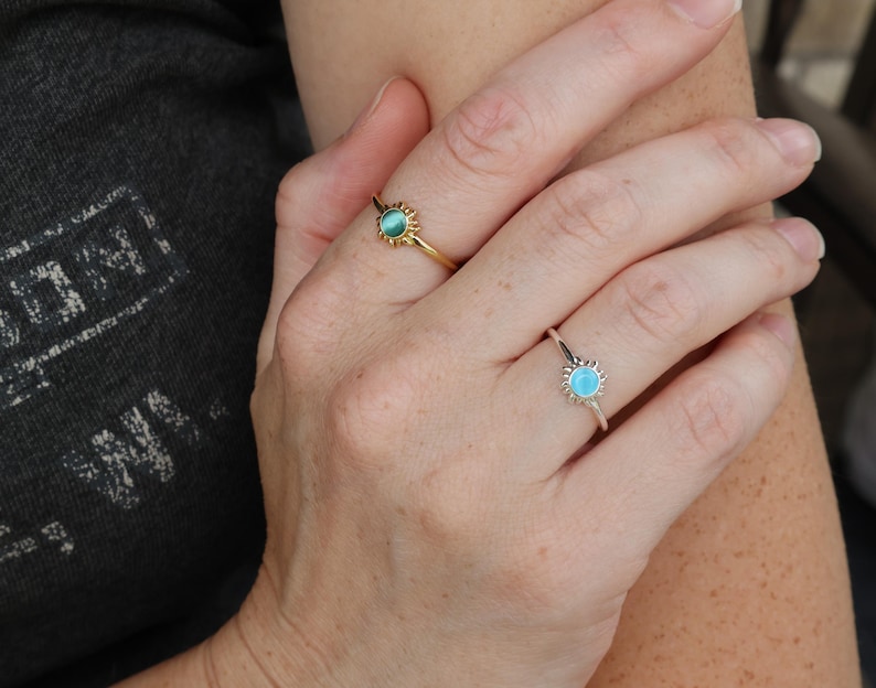 May include: Two rings with a sun design and a turquoise stone. The ring on the left has a gold band and a green stone. The ring on the right has a silver band and a blue stone.
