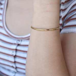 May include: A thin gold bangle bracelet on a person's wrist.