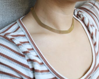 May include: A gold chain necklace with a mesh design. The necklace is worn by a person with a striped shirt.