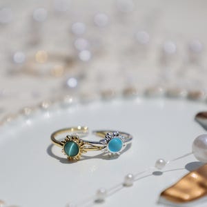 May include: Two gold and silver rings with blue and green gemstones. The rings are in the shape of a sun with a circular gemstone in the center.