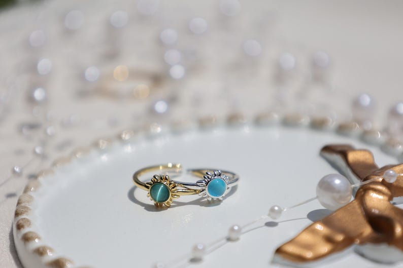 May include: Two gold and silver rings with blue and green gemstones. The rings are in the shape of a sun with a circular gemstone in the center.