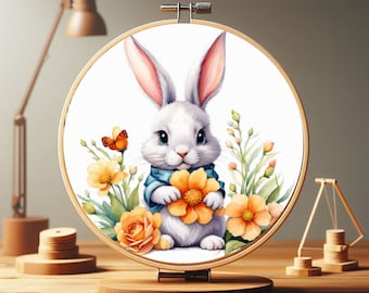 May include: A white rabbit with blue eyes holds a yellow flower in a floral embroidery hoop. The rabbit is wearing a blue shirt with white trim. The hoop is made of wood and has a white background.
