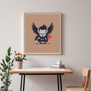 May include: Framed artwork showing a pixelated illustration of a dark creature with large black wings, yellow eyes, and a red apple. The artwork is in a wooden frame and hangs on a beige wall. The artwork is displayed above a wooden desk.