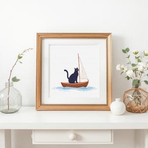 May include: A framed illustration of a black cat sitting in a small sailboat on the water. The cat is looking to the right. The sailboat has a white sail.